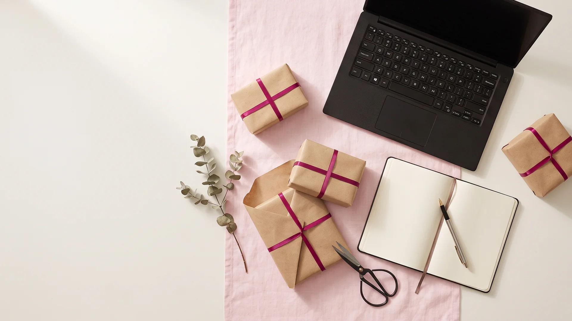 Desk with laptop, a handwritten shortlist, and small wrapped parcels while planning a gift guide