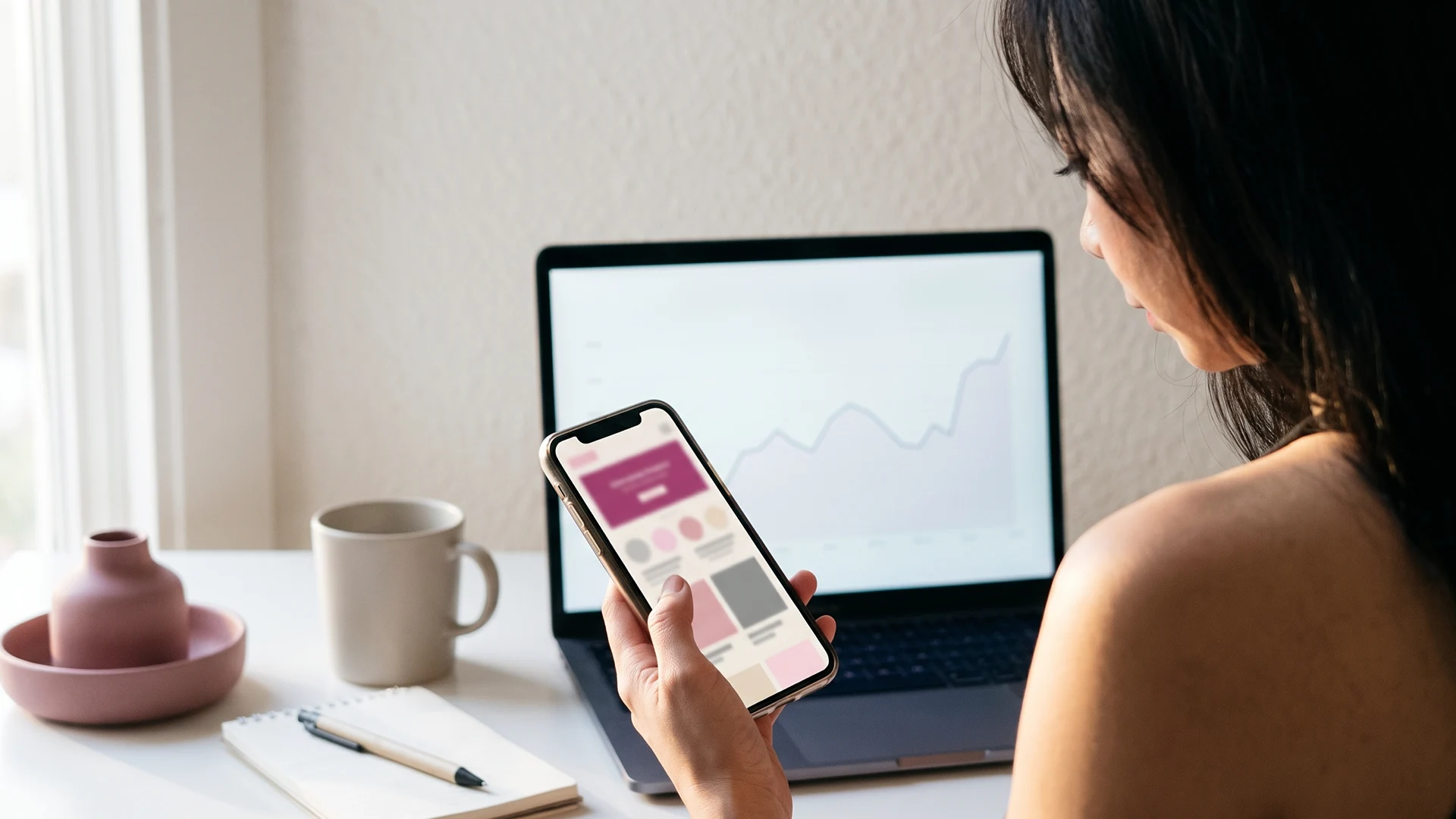 Shopify store owner checking her own store on a phone beside a laptop showing session data