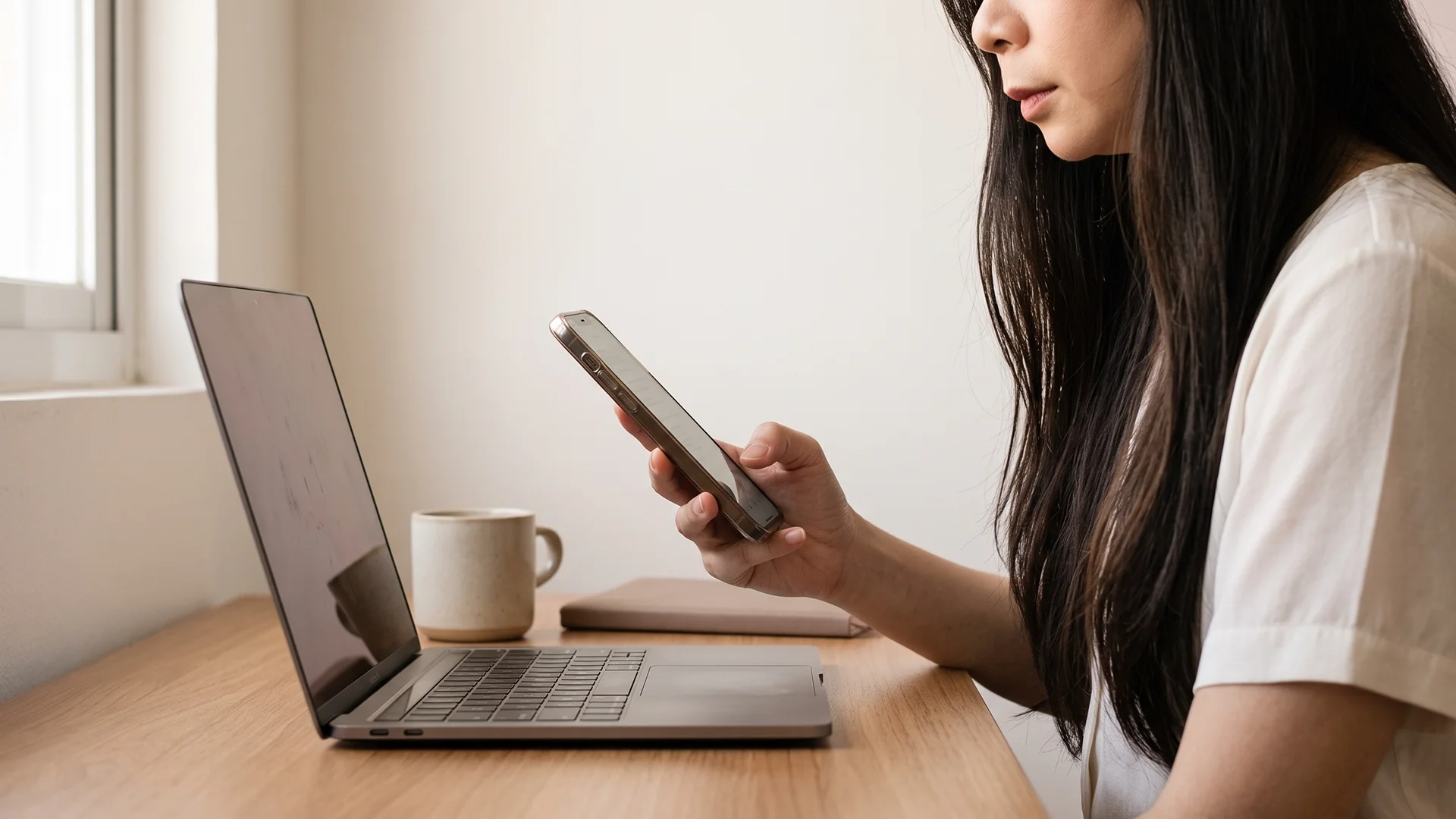 Shopify store owner checking a WhatsApp chatbot thread on her phone beside an open laptop